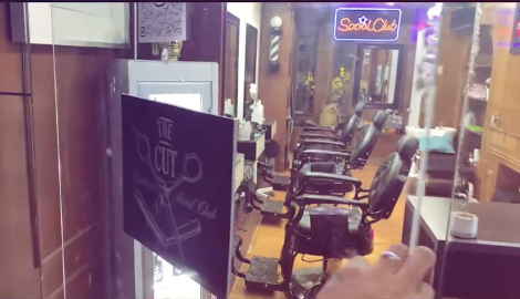 Interior de The Cut: sillones de barbero negros frente a espejos, piso de madera y el letrero de neón Social Club al fondo